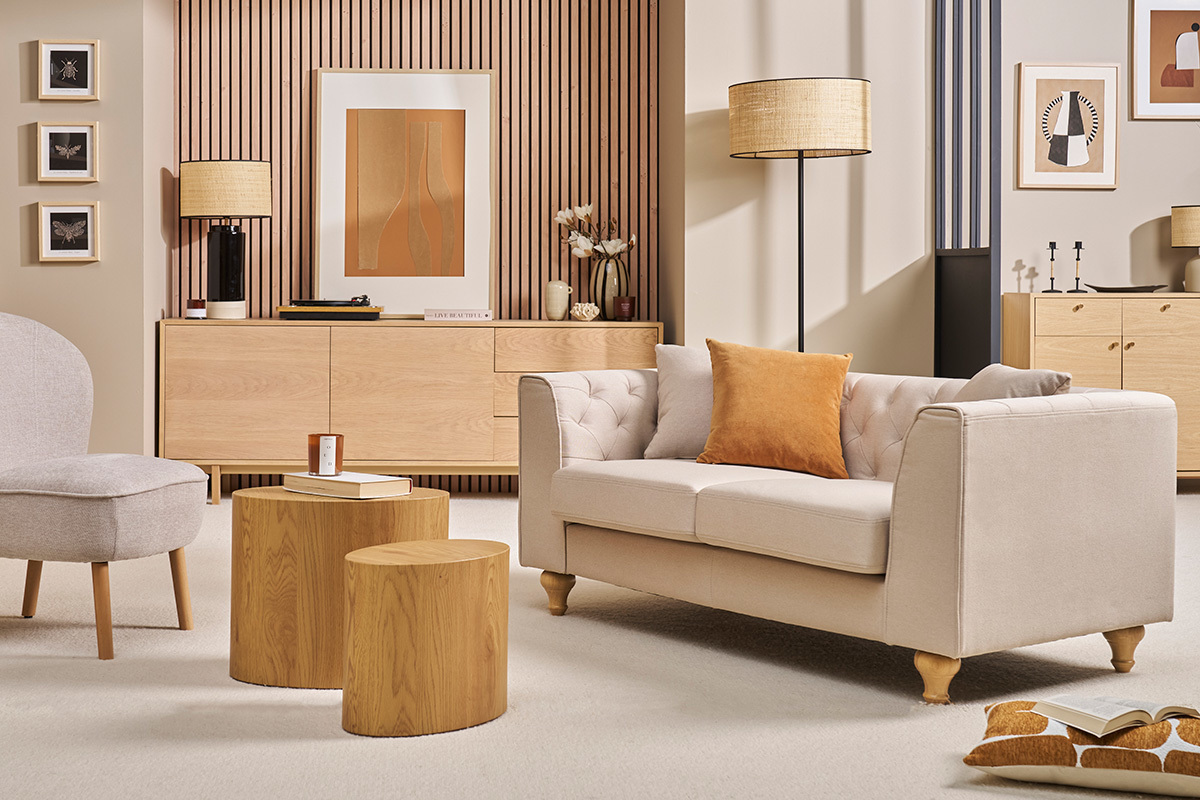 Sof de 2 plazas capiton beige MONTAIGNE en tela, vista lateral con cojn naranja, en un saln elegante.