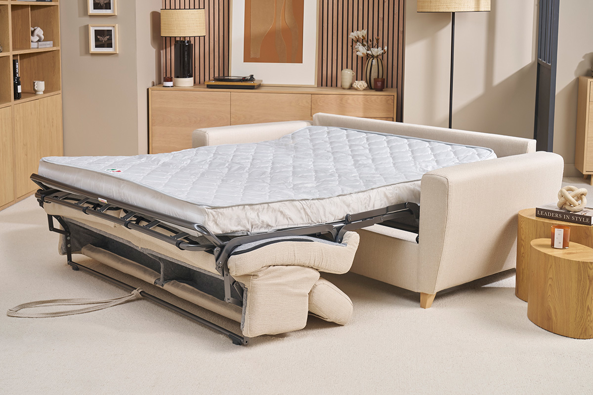 Sof cama convertible beige con colchn desplegado en una sala de estar.