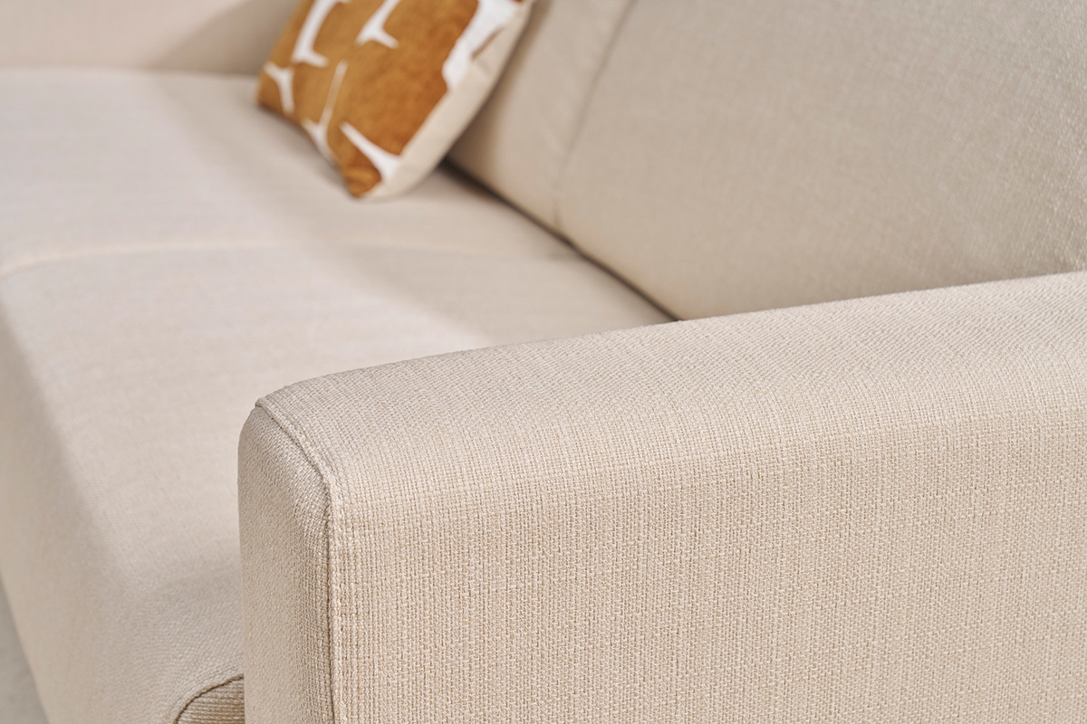 Apoyabrazos de un sof beige de tela con cojn decorativo. Vista de cerca.