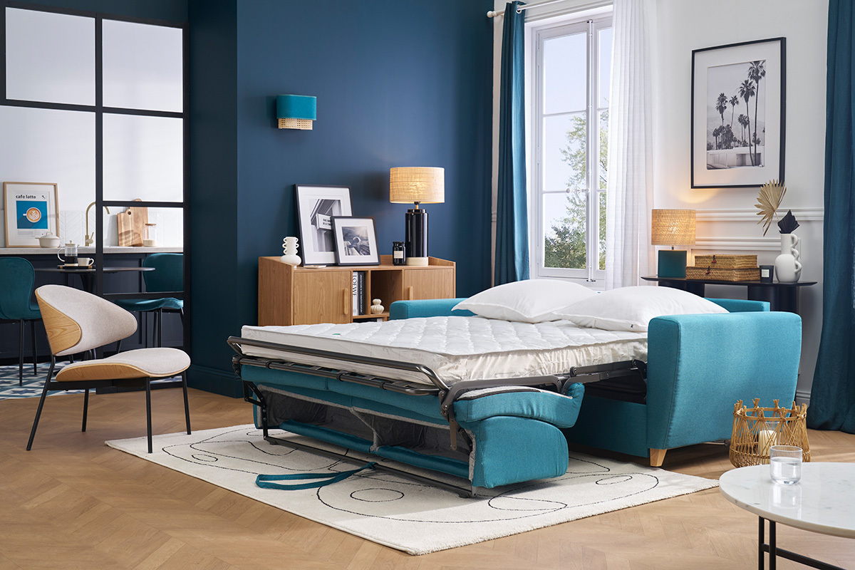 Sof� cama azul petr�leo abierto con colch�n en un sal�n moderno.