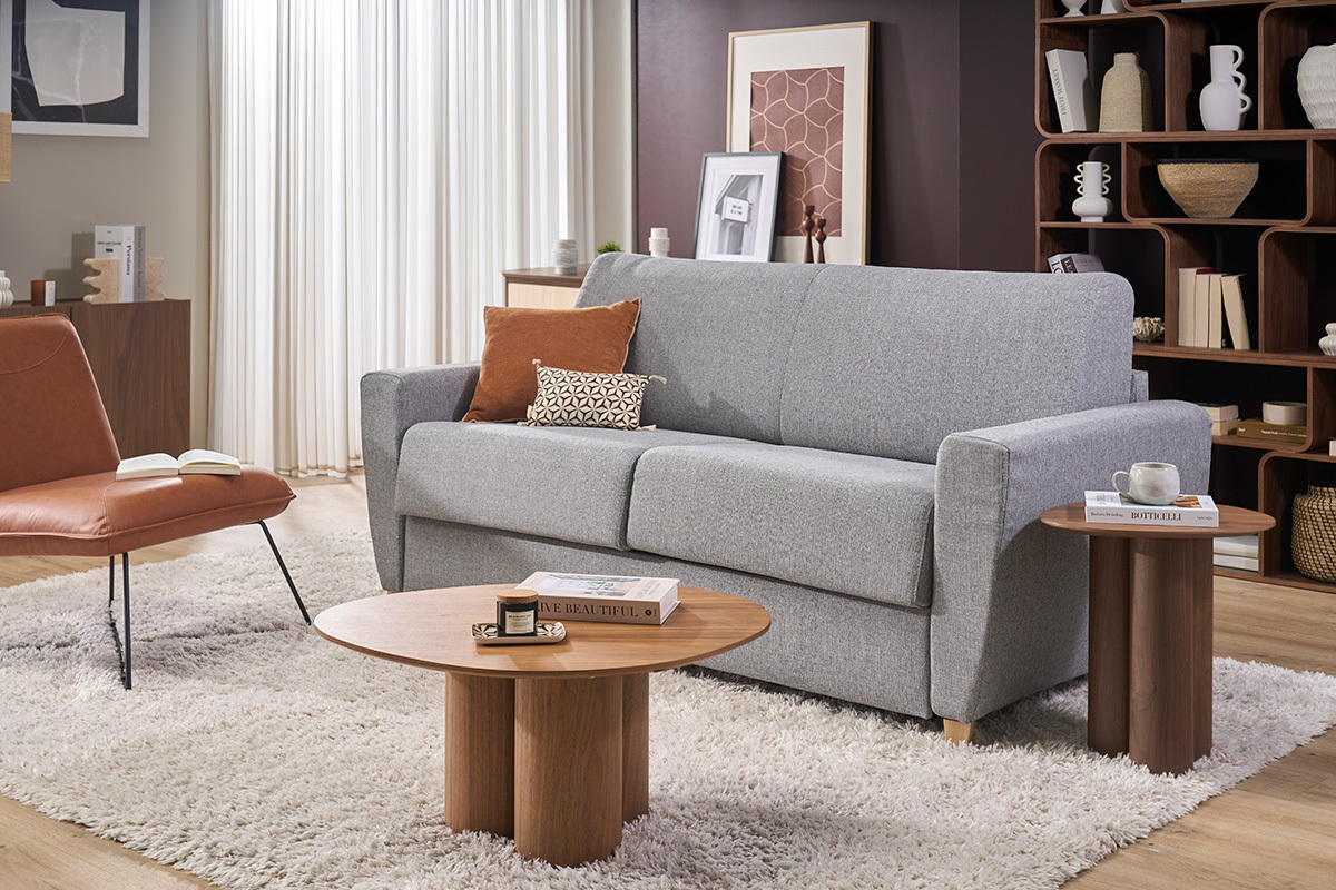 Canap� convertible GRAHAM en tejido gris claro con cojines, acompa�ado de mesas bajas, vista frontal.