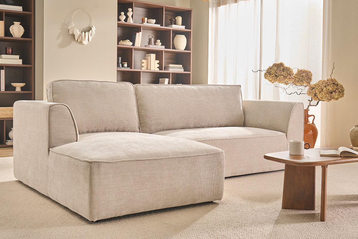 Sof� de esquina izquierdo de tela beige con mesa de centro en un sal�n luminoso.