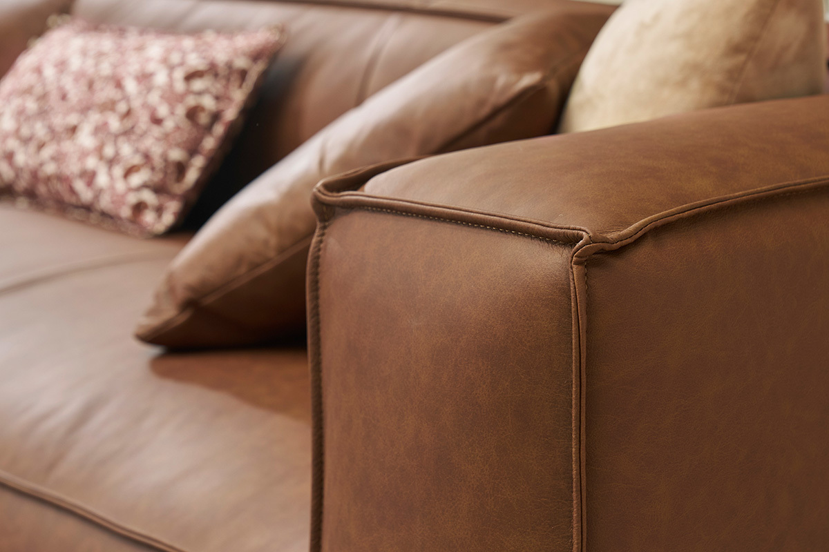 Brazo de sof esquinero de cuero marrn con cojines.