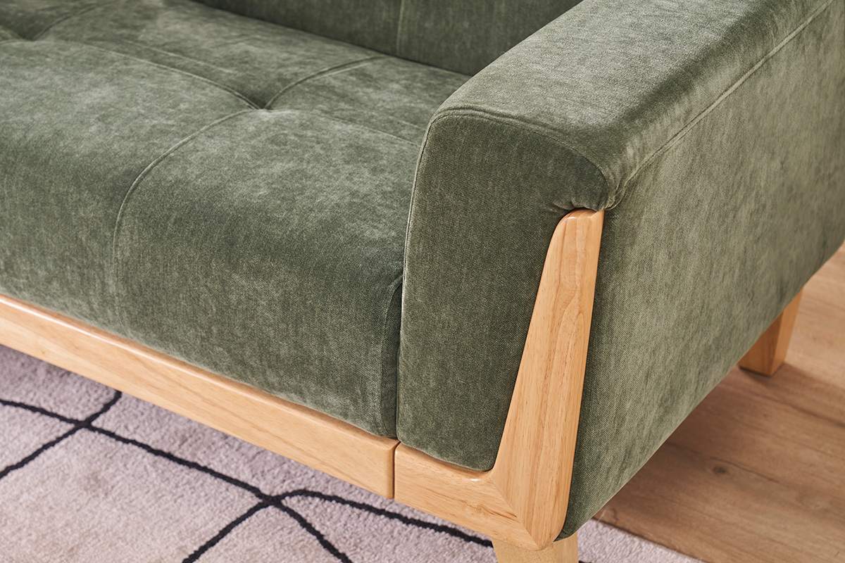 Detalle de un sof� escandinavo verde caqui de tela efecto terciopelo con reposabrazos de madera clara.
