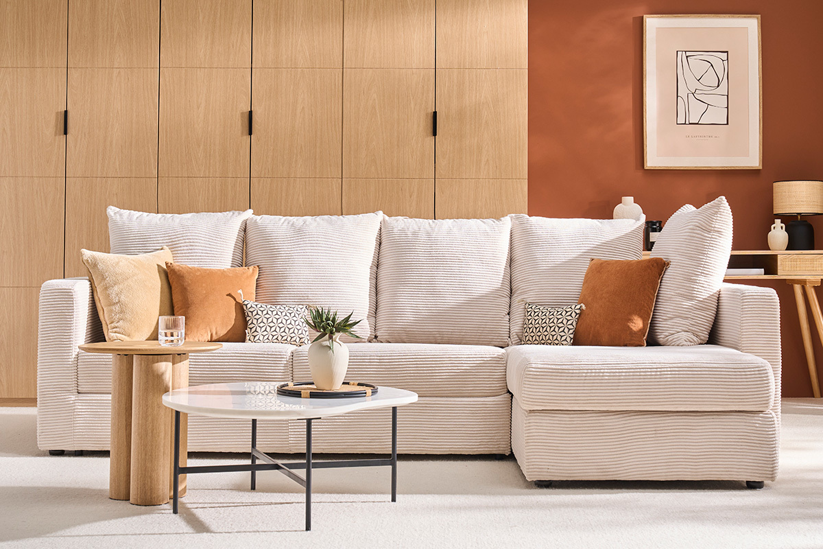 Sof esquinero convertible en pana beige, cojines a juego, mesa de centro y planta, fondo de madera clara.