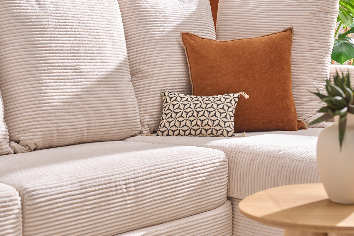 Sof de esquina beige de pana con cojines decorativos visto de lado.