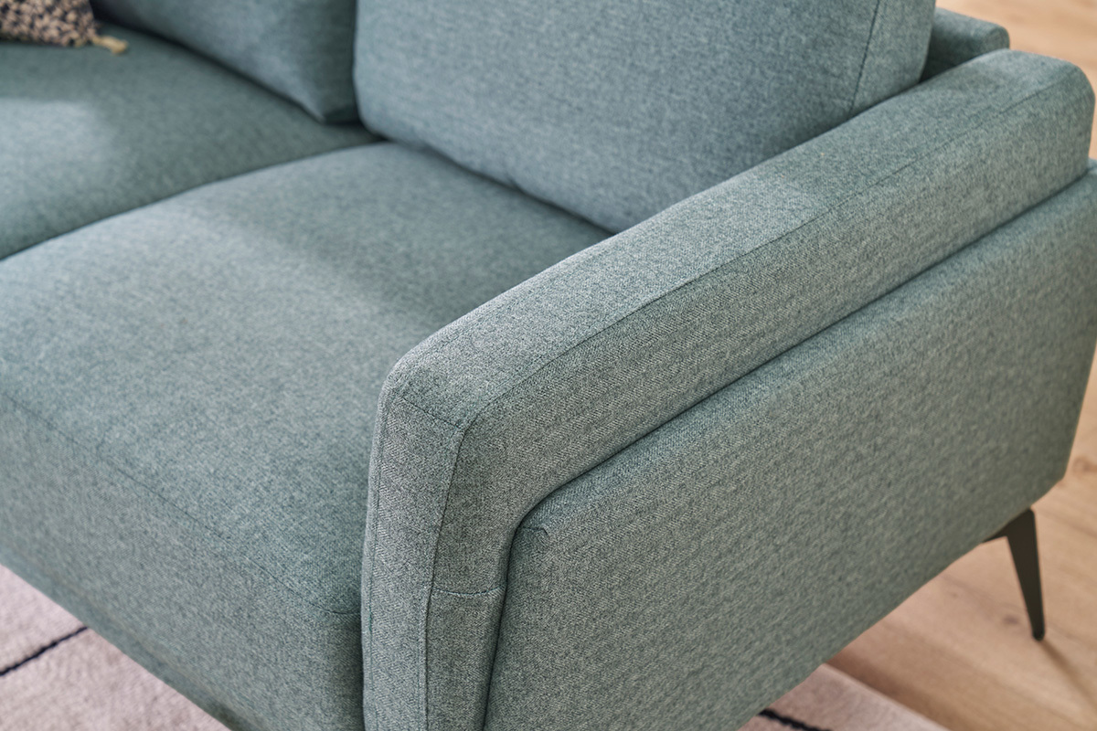 Sof� de 2 plazas en tela verde gris�ceo con patas de metal negro, vista cercana del reposabrazos.