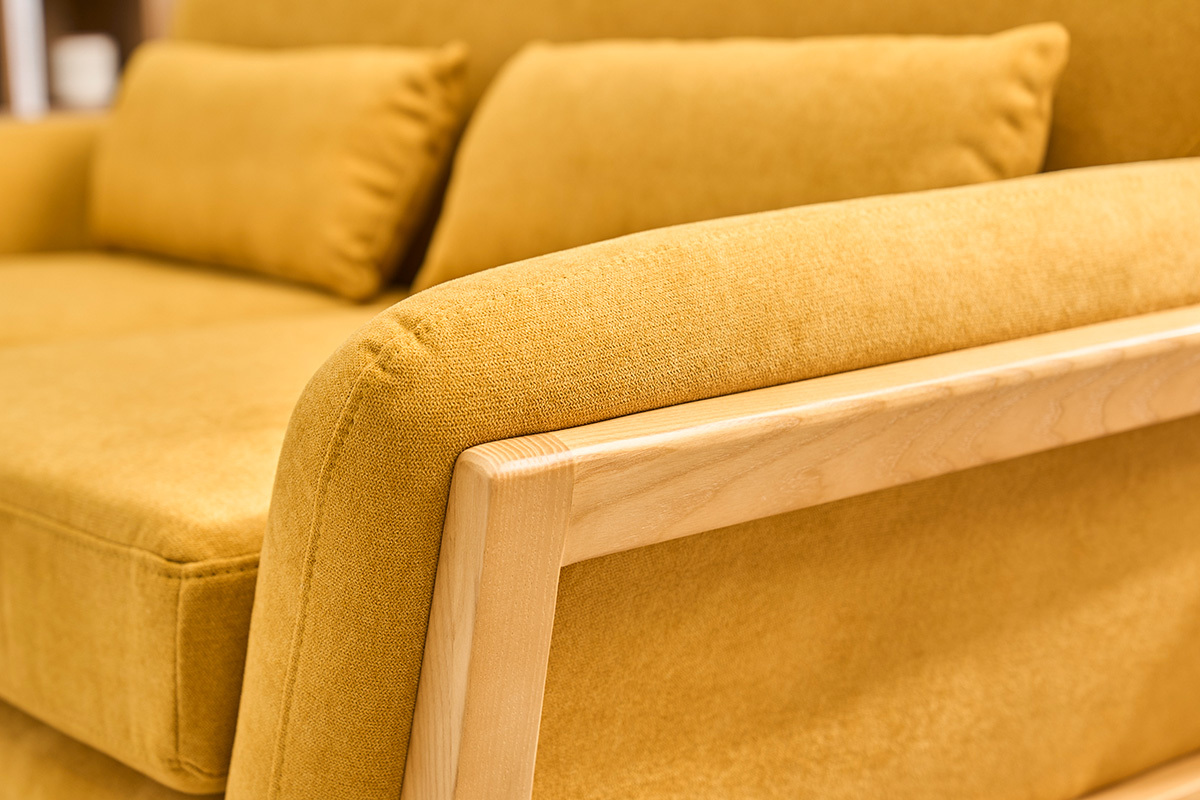 Detalle de un sof� escandinavo de 2 plazas en tela amarillo mostaza con reposabrazos de madera clara.