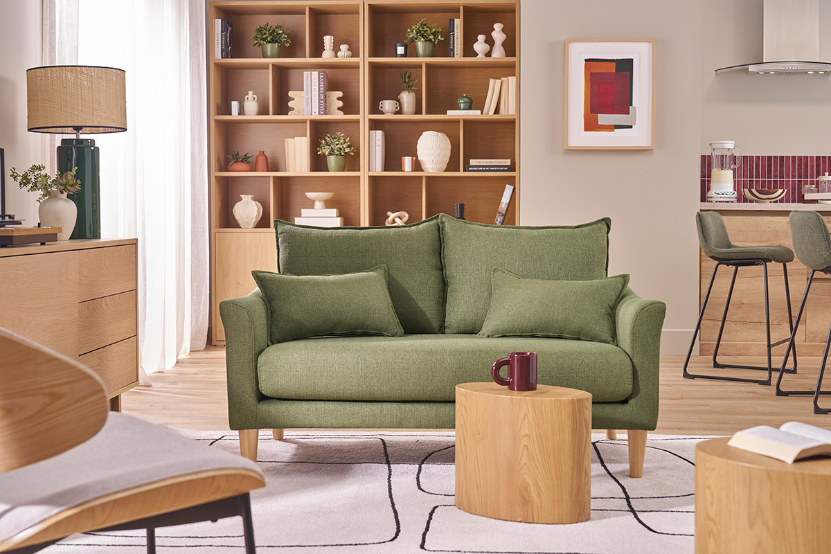 Sof� de 2 plazas de tela verde caqui con patas de madera, ubicado en un sal�n luminoso.