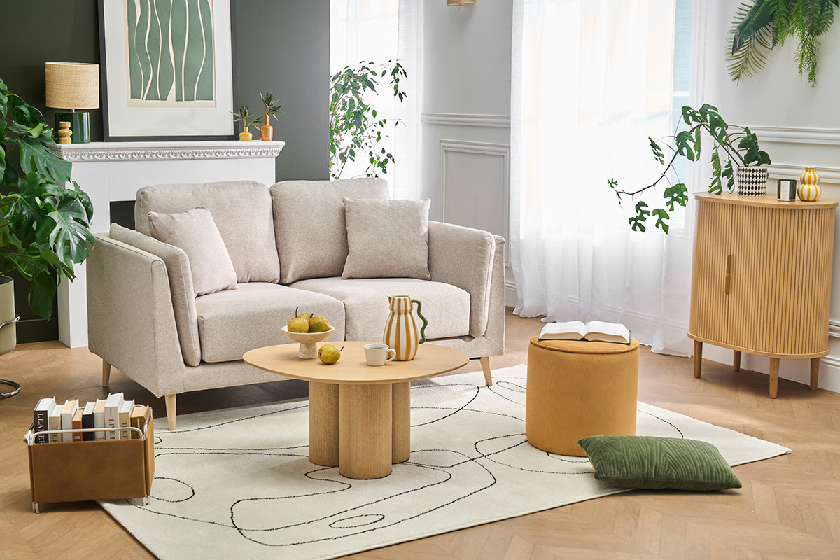 Sof� escandinavo para 2 plazas beige con cojines, mesa y accesorios decorativos en una sala luminosa.