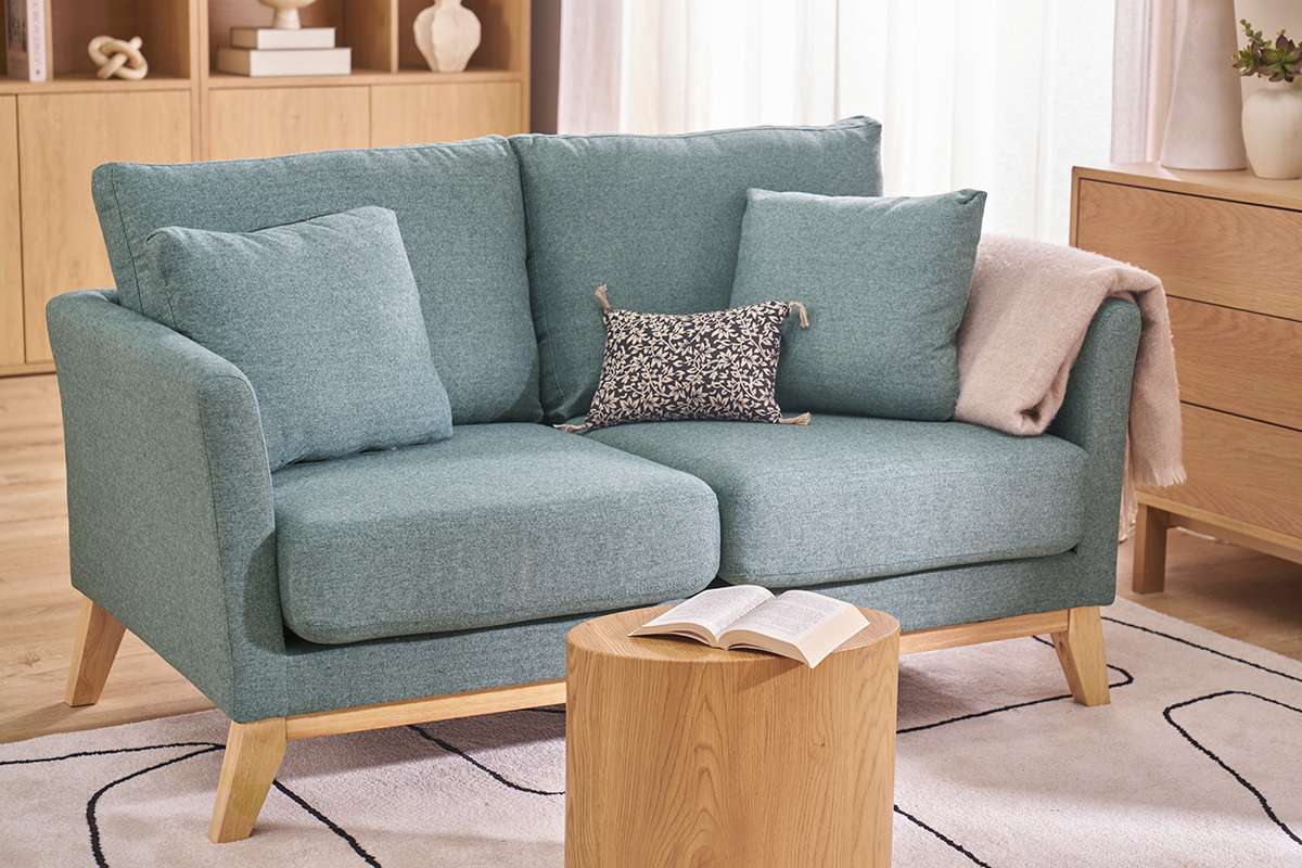 Sof� escandinavo verde gris�ceo de 2 plazas con cojines, mesa baja enfrente.