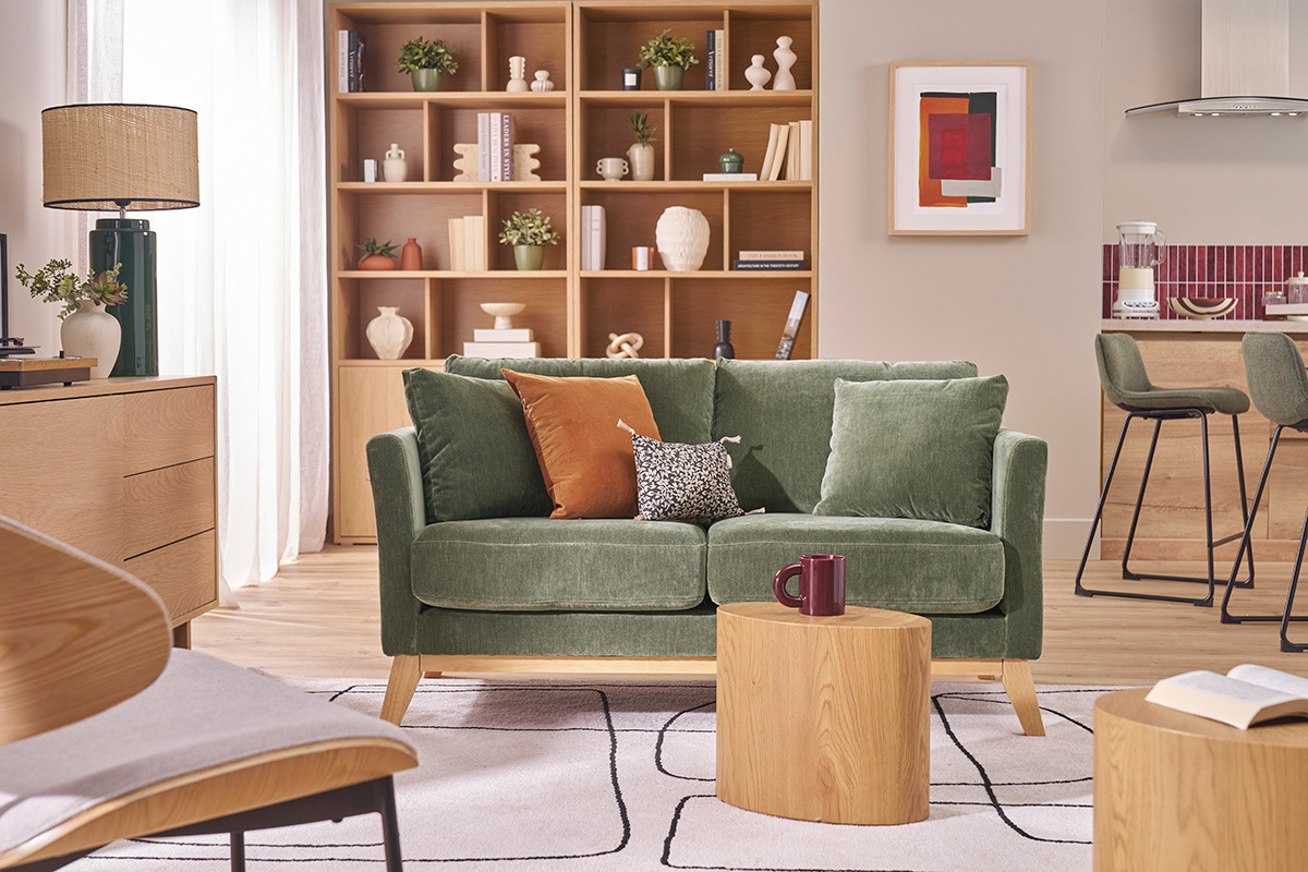 Sof� escandinavo de 2 plazas en verde kaki Oslo, con patas de madera, en un sal�n con mesa de madera y estantes.