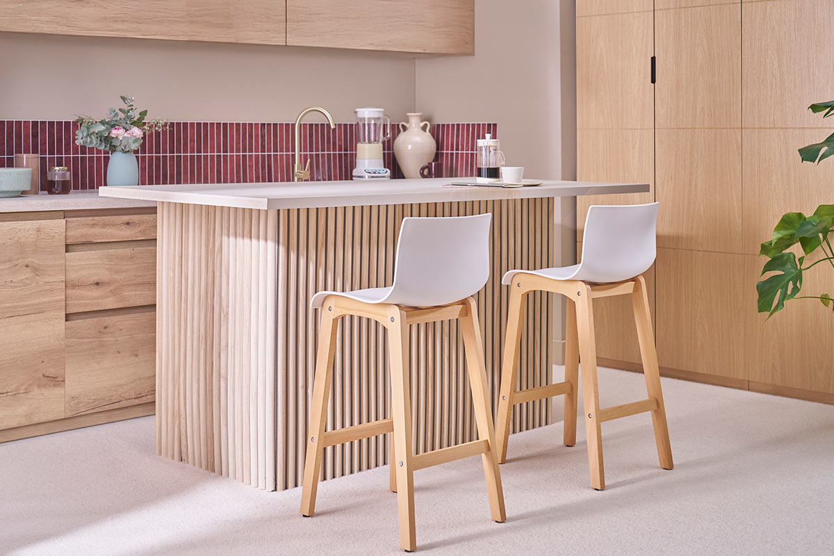 Dos taburetes de bar de madera y blanco, con respaldo, colocados frente a una isla central en la cocina.