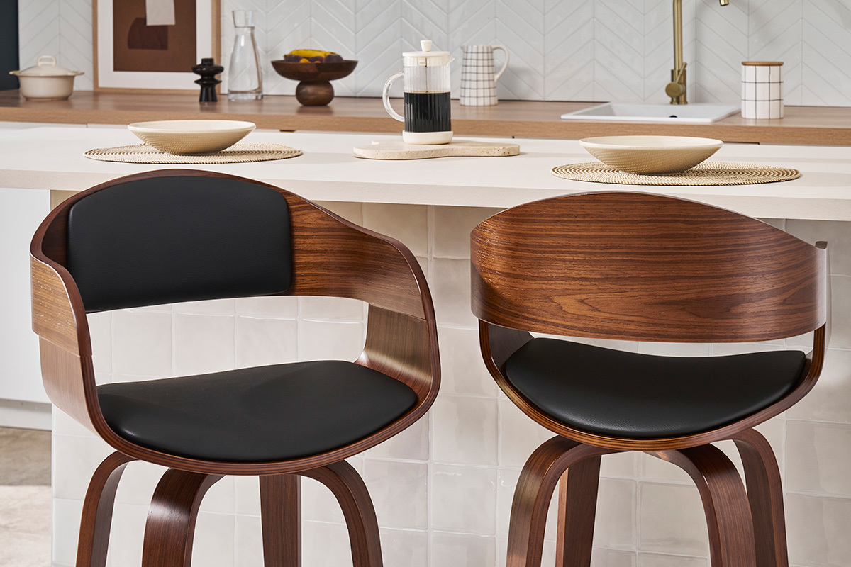 Dos taburetes de bar de nogal con asiento de poliuretano negro, frente a un mostrador de cocina.