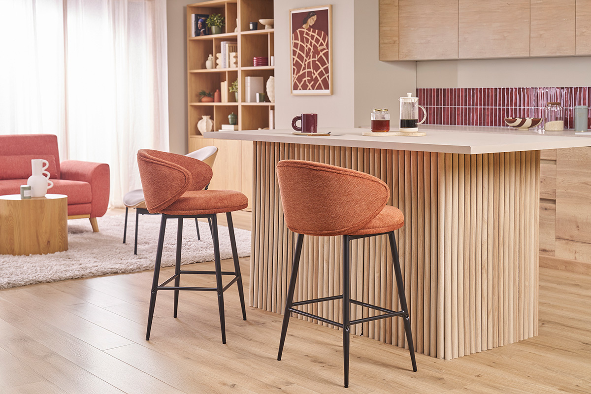 Taburetes de bar en tela color tierra quemada y metal negro frente a una isla central de madera.