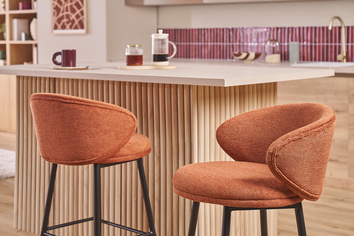 Dos taburetes de bar de tela color tierra quemada con patas met�licas negras frente a una isla de cocina.