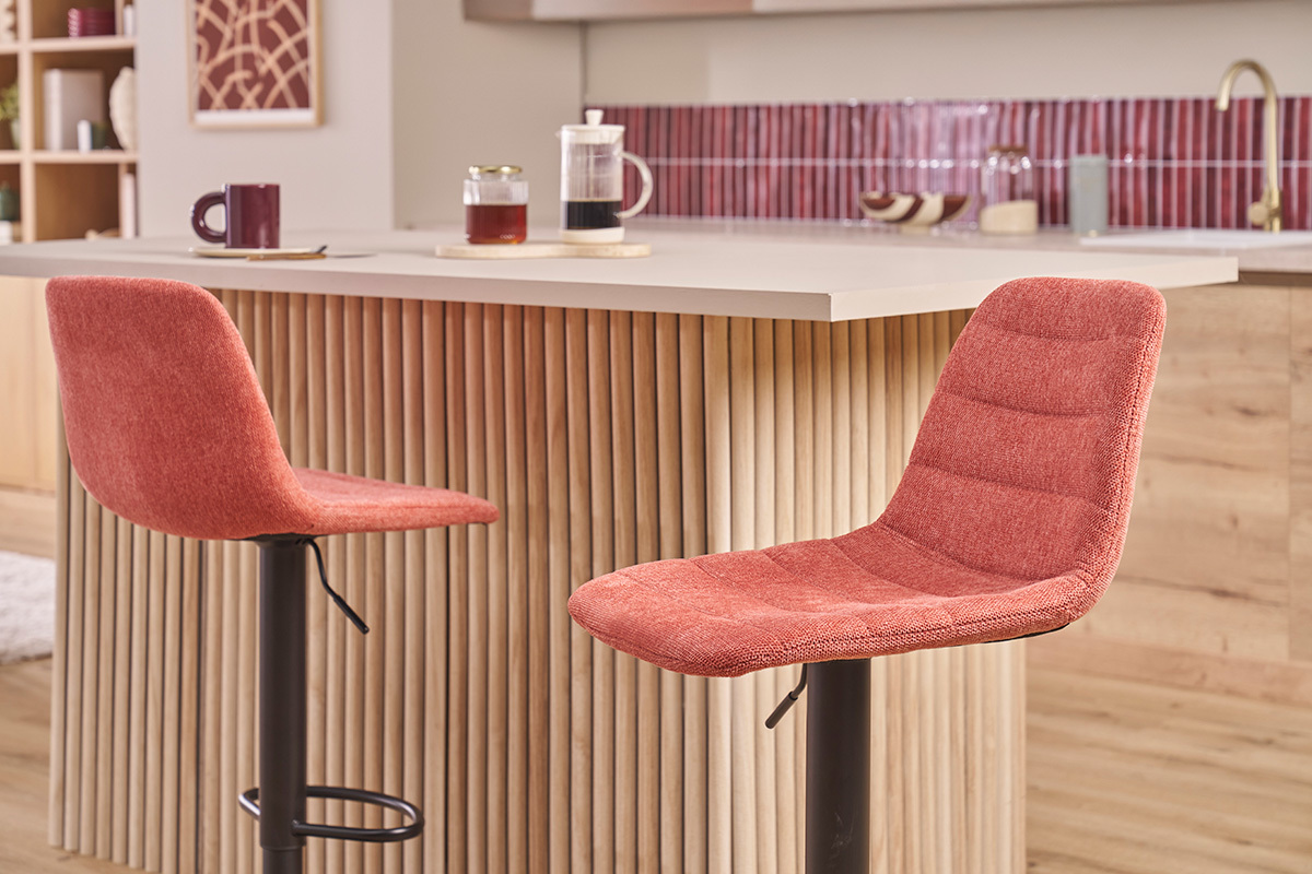 Dos taburetes de bar de tela terracota con patas de metal negro frente a una isla de cocina.