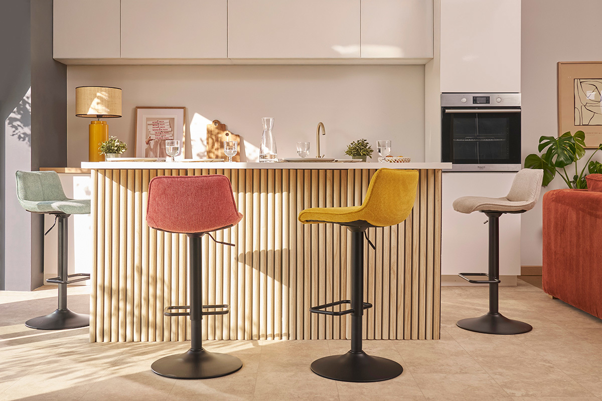 Cocina con taburetes de bar de tela efecto terciopelo y metal negro alrededor de un mostrador.