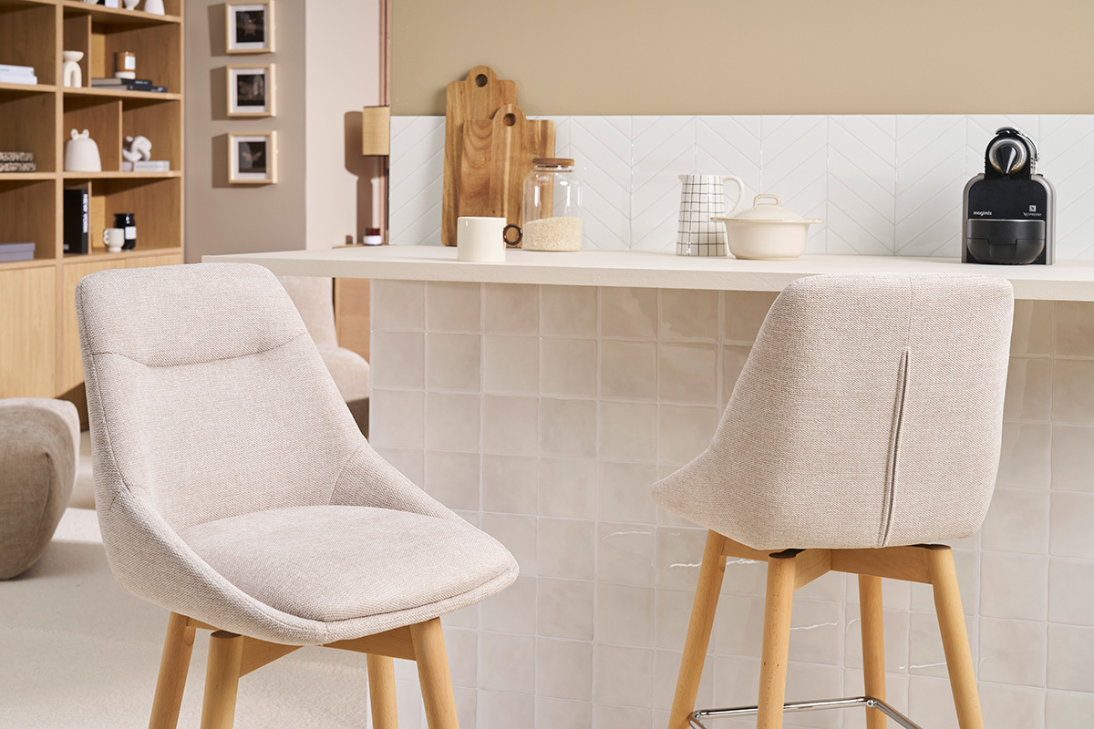 Dos taburetes de bar escandinavos de tela beige y madera clara frente a un mostrador de cocina.