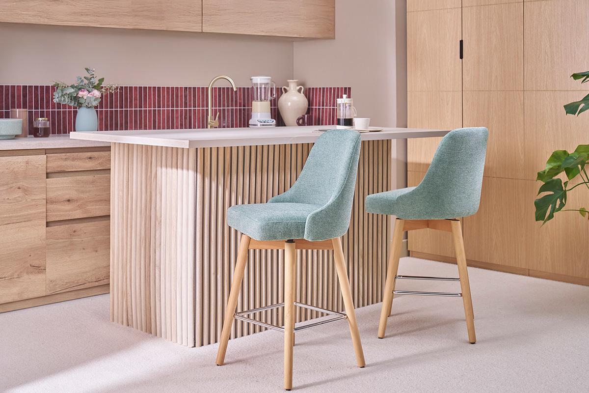 Dos taburetes de bar verdes y de madera frente a un mostrador de cocina.