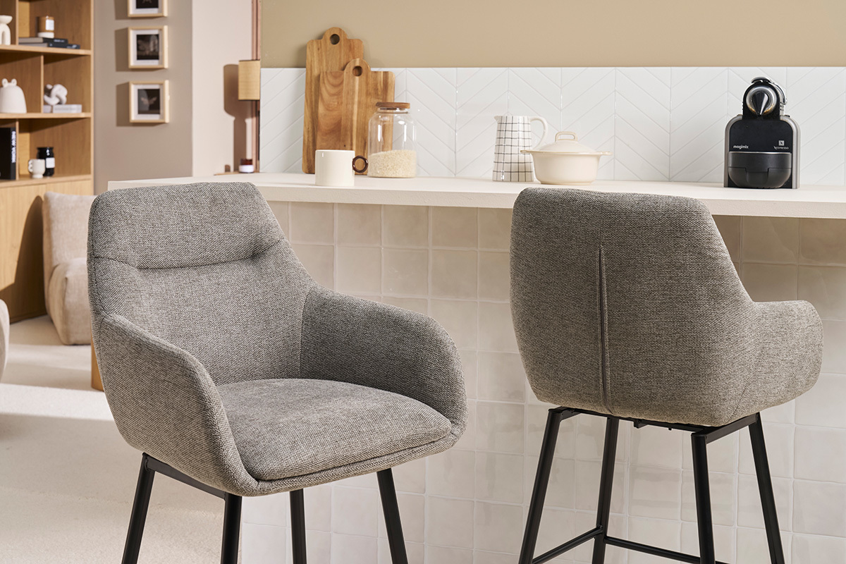 Dos sillas de bar grises de tela vistas de perfil y de espaldas frente a un mostrador.